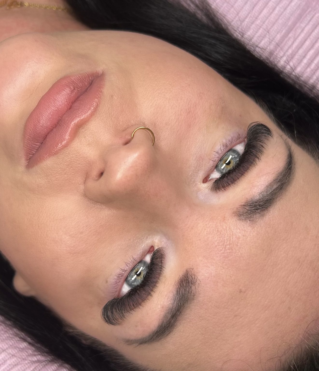 A client lying back on the pink treatment bed with fresh lashes and shaped brows