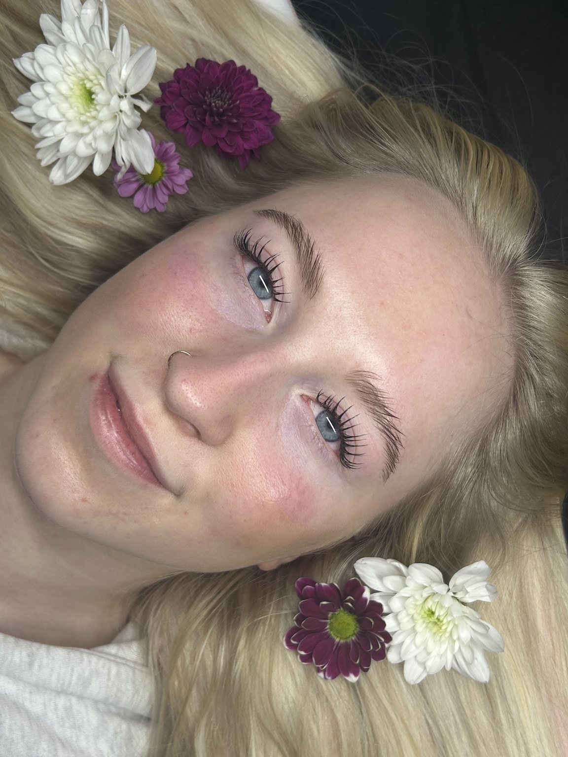 A natural lash set on a client with blonde hair, flowers around her